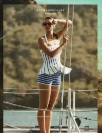 An Anthropologie catalog placed on a wooden coffee table with a ceramic mug and a cozy linen throw blanket nearby.