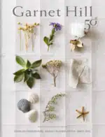 A stack of high-quality organic cotton bedding and a cashmere sweater representing the products found in the Garnet Hill catalog.