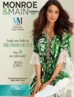 A stylish woman wearing a colorful dress from the Monroe & Main catalog standing in a brightly lit room.